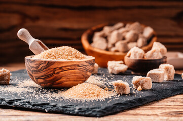 Bowl and scoop with sand and lump brown sugar on wooden background. brown sugar cube. Make...