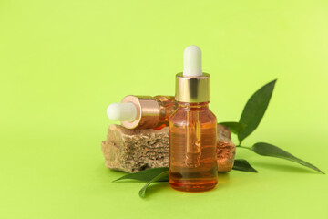 Bottles of natural serum, stone and plant leaves on green background