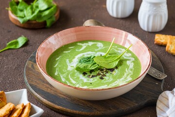 Summer spinach soup with cream in a pink plate on a wooden board on a brown concrete background....
