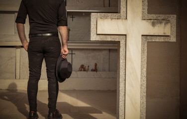 Adult man in black holding hat mourning in cemetery