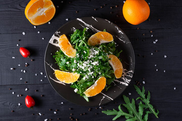 Fototapeta na wymiar fruit salad of oranges and arugula leaves on a black wooden background