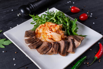 roast beef tongue with lettuce, cabbage and arugula leaves on a black wooden background