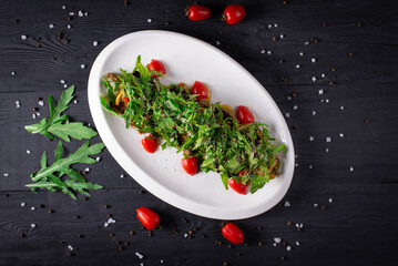 salad with meat, tomatoes and arugula on a black wooden background