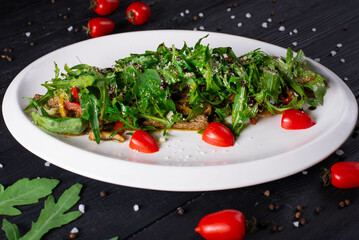 salad with meat, tomatoes and arugula on a black wooden background