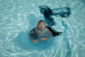 art portrait of asian woman underwater in the swimming pool in blue dress