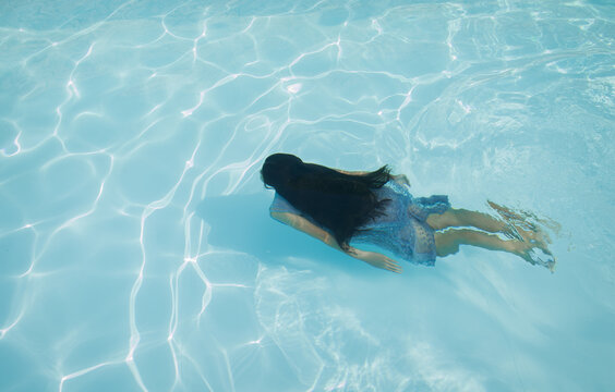 art portrait of girl in blue dress swimming underwater in the pool