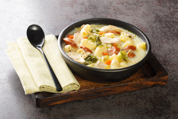 Filipino chicken soup with elbow pasta, vegetables, sausages close-up in a bowl on a wooden tray....