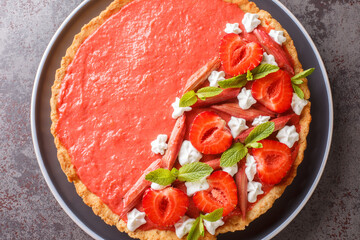 Summer dessert tart with strawberries, rhubarb, mint and whipped cream close-up on a plate on the table. Horizontal top view from above