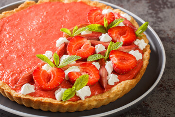 Summer dessert tart with strawberries, rhubarb, mint and whipped cream close-up on a plate on the table. Horizontal