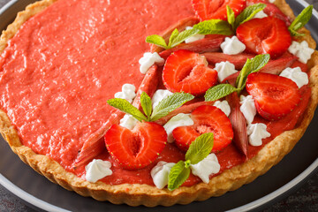 Delicious berry tart with strawberries, rhubarb, mint and whipped cream close-up on a plate on the table. Horizontal