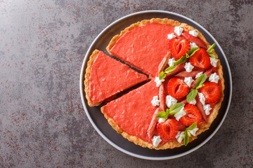 Sliced strawberry and rhubarb tart decorated with mint and whipped cream close-up on a plate on the table. Horizontal top view from above