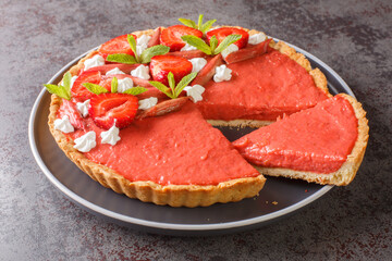 Sliced strawberry and rhubarb tart decorated with mint and whipped cream close-up on a plate on the...