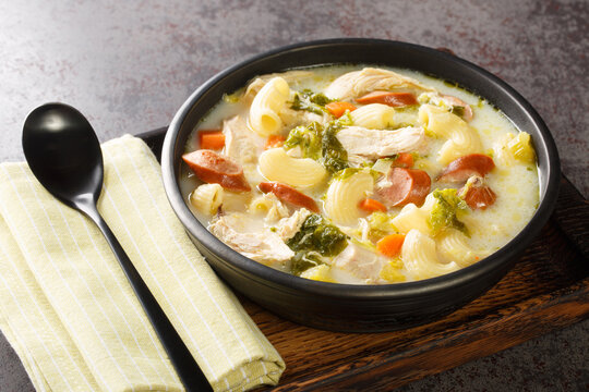 Creamy Chicken Sopas is a Filipino soup with pasta, vegetables, sausages and chicken close-up in a bowl on a wooden tray. Horizontal