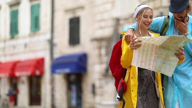 A young couple is using a map while walking the old city during a holiday on a rainy day on the seaside. Vacation, tourists, relationship, seaside