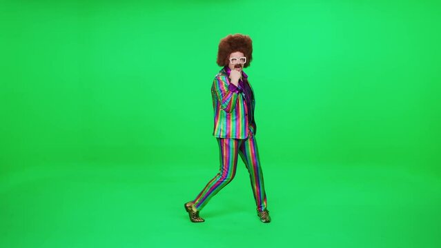 Retro dude in a multicolored suit dancing a funny dance on a green background, a festive mood, a retro disco man is having fun at a new year's party.