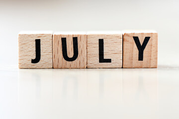 JULY word arranged with wooden letters on a light background.