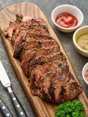 Grilled sliced beef steak on cutting board over grey table. Chuck tenderloin steak