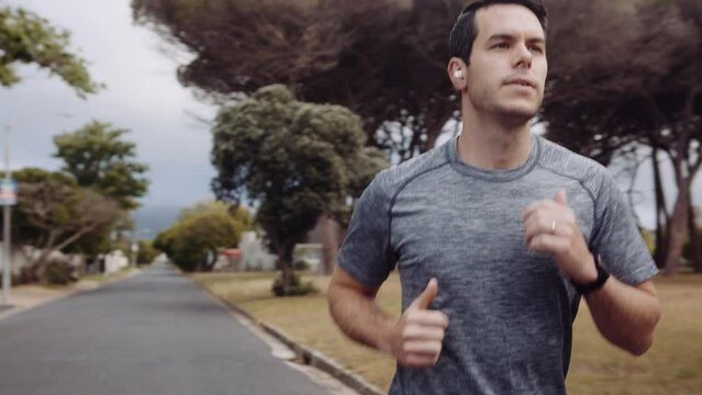 Caucasian man jogging in the street of a residential area with earphones in his ears.