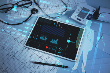 Close up of doctor's desktop with pad, stethoscope and glowing online medicine hologram. Healthcare, future and technology concept. Double exposure.