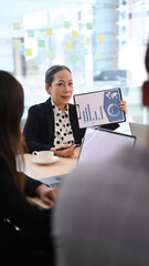 Senior female team leader holding digital tablet and giving presenting new marketing strategy at board room