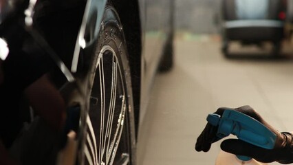 Man with spray cleans car wheels 