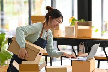 Smiling young asian woman online seller checking product purchase order on laptop computer. E-Commerce, online business, online sales concept