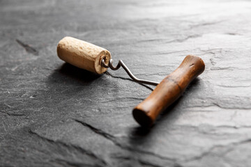 Vintage wine corkscrew in a cork on a black slate background. - obrazy, fototapety, plakaty
