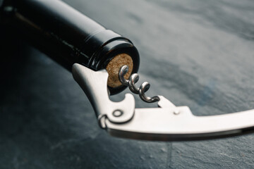 Stainless  wine corkscrew in a cork of wine bottle neck on a black rocky slate background