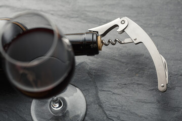 Stainless  wine corkscrew in a cork of wine bottle neck on a black rocky slate background - obrazy, fototapety, plakaty