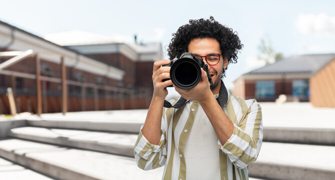 photography, profession and people and concept - happy smiling man or photographer in glasses with digital camera over city street background