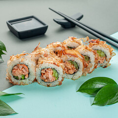 Sushi roll Bonito in tuna shavings. With fried salmon and cucumber. Decorated with greenery. In the background is a gravy boat and chopsticks. Close-up.