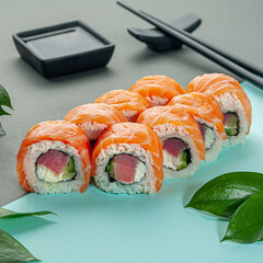 Sushi roll with salmon and tuna. Decorated with greenery. In the background is a gravy boat and chopsticks. Close-up.