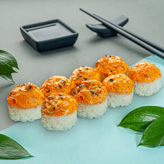 Baked sushi roll with mussels, cream cheese and spicy sauce. Decorated with greenery. In the background is a gravy boat and chopsticks. Close-up.