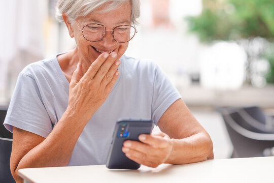 Attractive Smiling Senior Woman Using The Phone Sitting At The Bar Table, Mature Lady Laughing In Video Chat