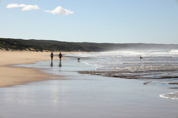 Fototapeta na wymiar Two females walking along a sandy beach at Witsand, Western Cape, South Africa.