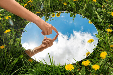 nature concept - hand touching sky reflection in round mirror on summer field - Powered by Adobe