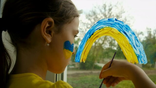 A child draws a Ukrainian rainbow on the window of the house. Selective focus.