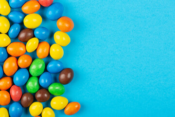 Colorful chocolate candies on blue background with copy space, top view, flat lay