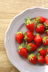 Lilac plate full of fresh strawberries on wooden table. Flat lay.