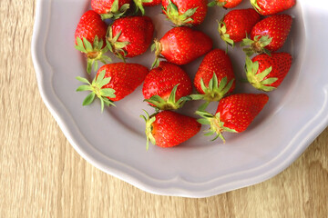 Lilac plate full of fresh strawberries on wooden table. Flat lay.