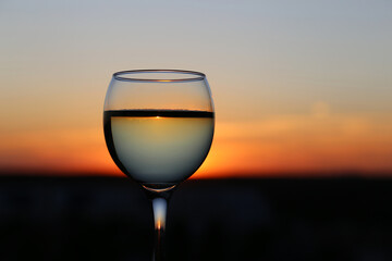 Glass with white wine on sunset sky background. Concept of celebration, wine industry