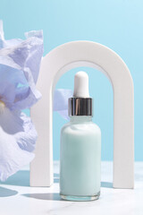 Obraz na płótnie Canvas Serum with floral extracts for skincare in arch. Nature cosmetics in glass bottle with pipette and iris flowers on blue background. Face and body care spa concept.