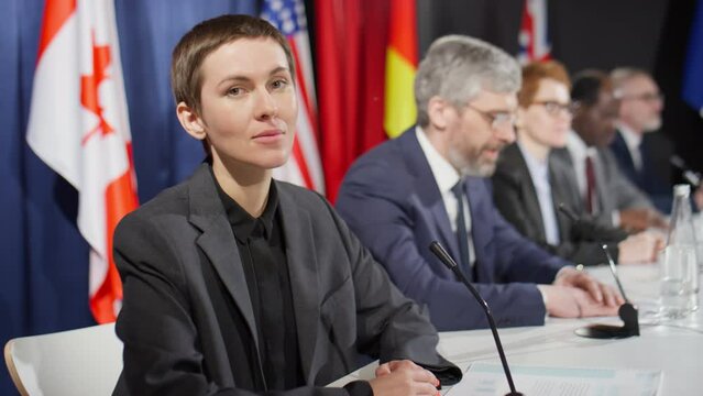 Portrait of young female diplomat with short brunette hair posing for camera at political press conference