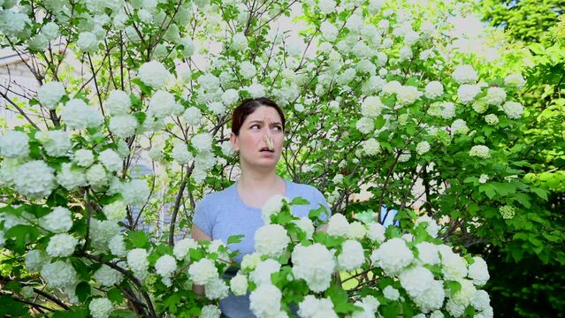 Unhappy woman stands with a clothespin on her nose near a flowering tree. Allergy. 
