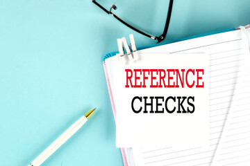 REFERENCE CHECKS text on a sticky on notebook with pen and glasses , blue background