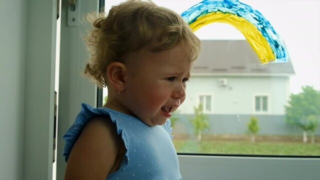 A child draws a Ukrainian rainbow on the window of the house. Selective focus.