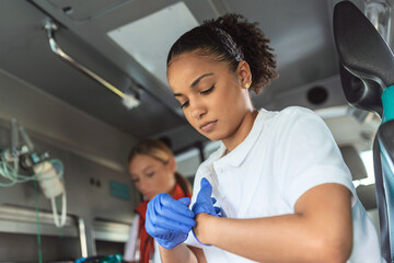 African american female paramedic taking off her gloves. Two paramedics helping injured patient