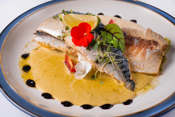 fish dish in sauce with lemon and herbs. on a white background
