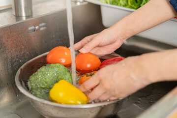 Close up asian young woman washing tomato, broccoli, carrot fresh vegetables, paprika with splash water in basin of water on sink in kitchen, preparing fresh salad, cooking meal. Healthy food people.