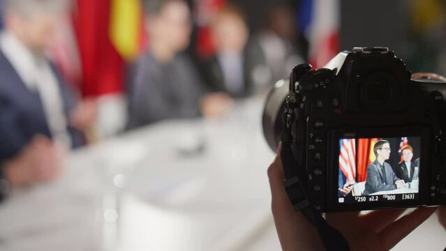 Selective focus close up shot of hands of unrecognizable journalist using professional camera while taking pictures of female politician holding speech at press conference
